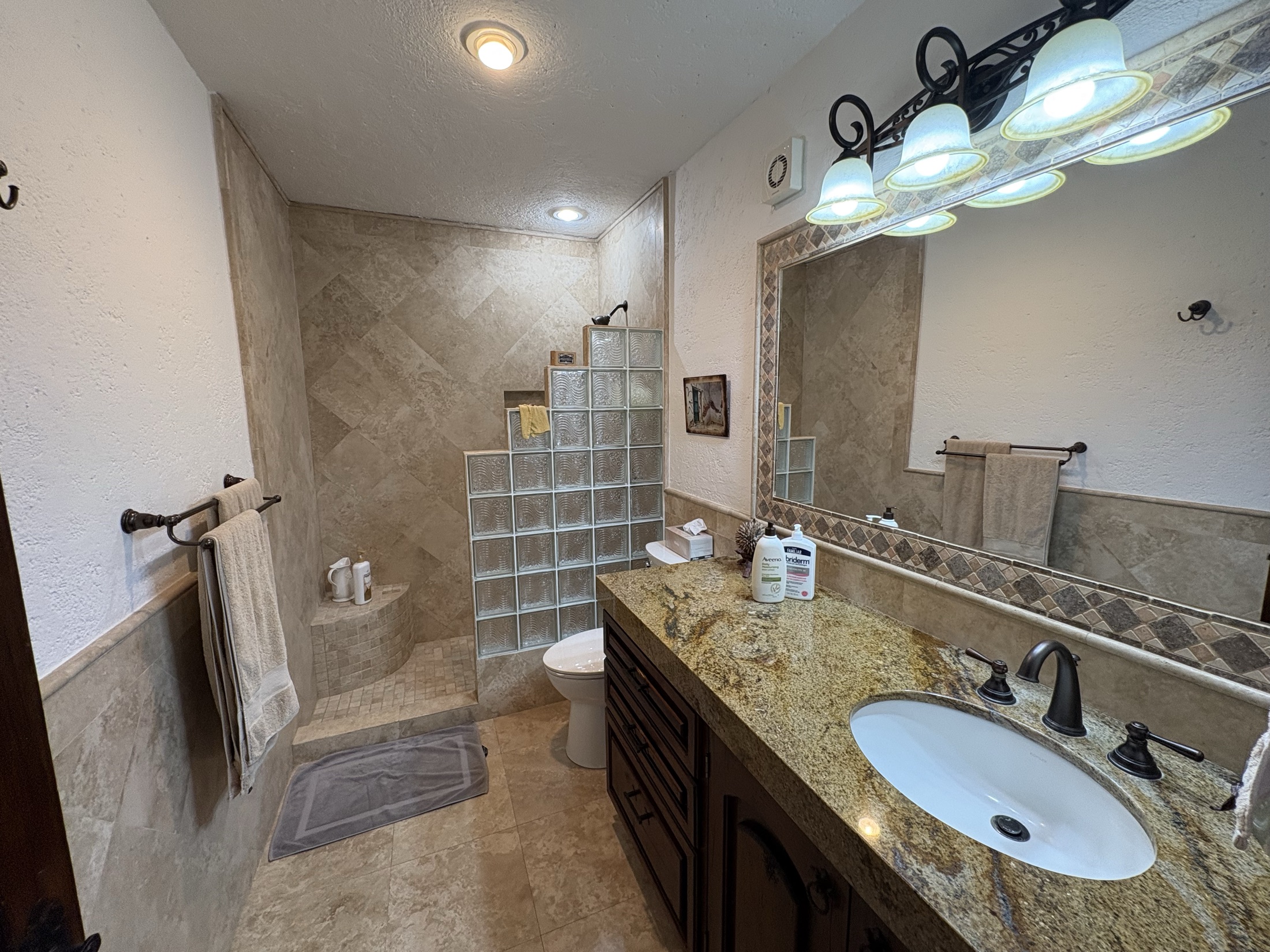 Bathroom with granite vanity, tiled shower, and glass block detail